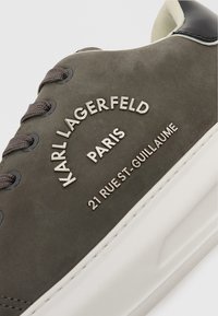 Γκρίζα σουέτ αθλητικά παπούτσια με λευκή ελαστική σόλα; διαθέτουν μεταλλικό λογότυπο, στρογγυλά κορδόνια και αντίθετη μαύρη λεπτομέρεια στη φτέρνα.