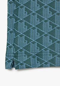 Mönstrad textil med geometrisk design i mörkgrön och ljusblå nyanser, med en mjuk textur och distinkta vinklade former.