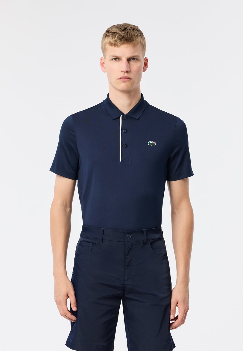 Polo shirt blu navy realizzato in tessuto liscio con abbottonatura a tre bottoni e rifiniture bianche a contrasto. Presenta un logo ricamato verde sul petto.
