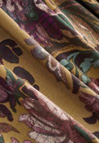 Tessuto con un motivo floreale in tonalità di viola, verde e marrone su un materiale morbido e testurizzato, con panneggi lisci e pieghe leggere.