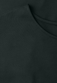 Gros plan sur un tissu vert foncé avec des coutures visibles et des coutures courbes, montrant la texture et les détails du vêtement.