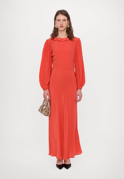 Ilga raudona suknelė su pūstomis rankovėmis, raukšlėtu apykakliu ir lengvai krentančia suknele. Modelis laiko raštuotą rankinę ir dėvi juodus smailius batus.