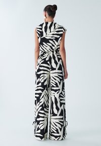 Melnbalts kombinezons ar lapu rakstu, bez piedurknēm, ar savilkta jostasvietu un platām kājām ar auklu akcentiem apakšā.