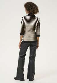 Randig stickad topp i svart och beige, med hög krage och trekvartsärmar, i kombination med högmidjade svarta läderbyxor.