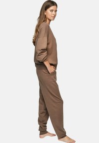Ensemble de détente en tricot marron comprenant un sweat-shirt ample avec des épaules tombantes et un pantalon ajusté assorti. Texture douce et accents côtelés.