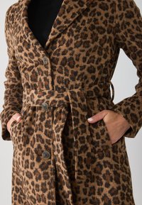 Leopardprintjas in bruin en zwart met een zachte textuur, een ceintuur rond de taille, grote knopen en zijzakken.