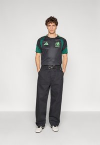 Black athletic shirt with green sleeves, featuring a textured design and a Mexico graphic. Worn with loose black pants and white shoes.