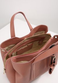 Vaaleanpunainen nahkakäsilaukku, jossa on kaksoiskahvat, sisäinen vetoketjullinen tasku ja vaalean beige kangasvuori, esitellään avoimena valkoisella pinnalla.