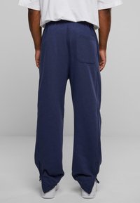 Marineblaue Sweatpants mit lockerer Passform, elastischem Bund, seitlichen Reißverschlussakzenten nahe den Bündchen und einer Rückentaschendetail.