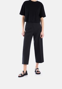 Sort cropped t-shirt kombineret med højtaljede sorte brede bukser og sorte flade sandaler med dobbelte remme.