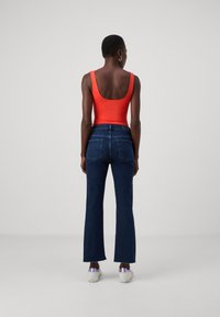 Felrood mouwloos topje gecombineerd met donkerblauwe flared jeans. De jeans hebben standaard achterzakken en een aangesloten taille.