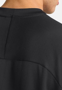 Zwarte sporttop met een textuur ribbelontwerp, gebogen naden en een ronde halslijn. Het materiaal lijkt glad met een lichte glans.