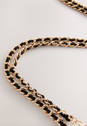 Kullatoonist kett-käevõru, millel on põimunud mustad kangasementide osad, keerutatud disain ja sile tekstuur.