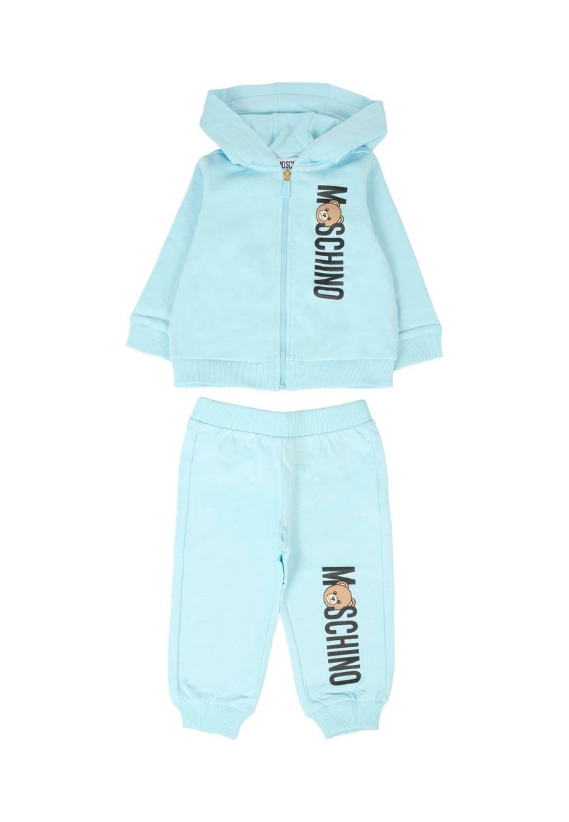 Jasnoniebieski zestaw dresowy z rozpinanym kapturem oraz dopasowanymi spodniami. Posiada logo "Moschino" i grafikę misia. Miękka tkanina, luźny krój.