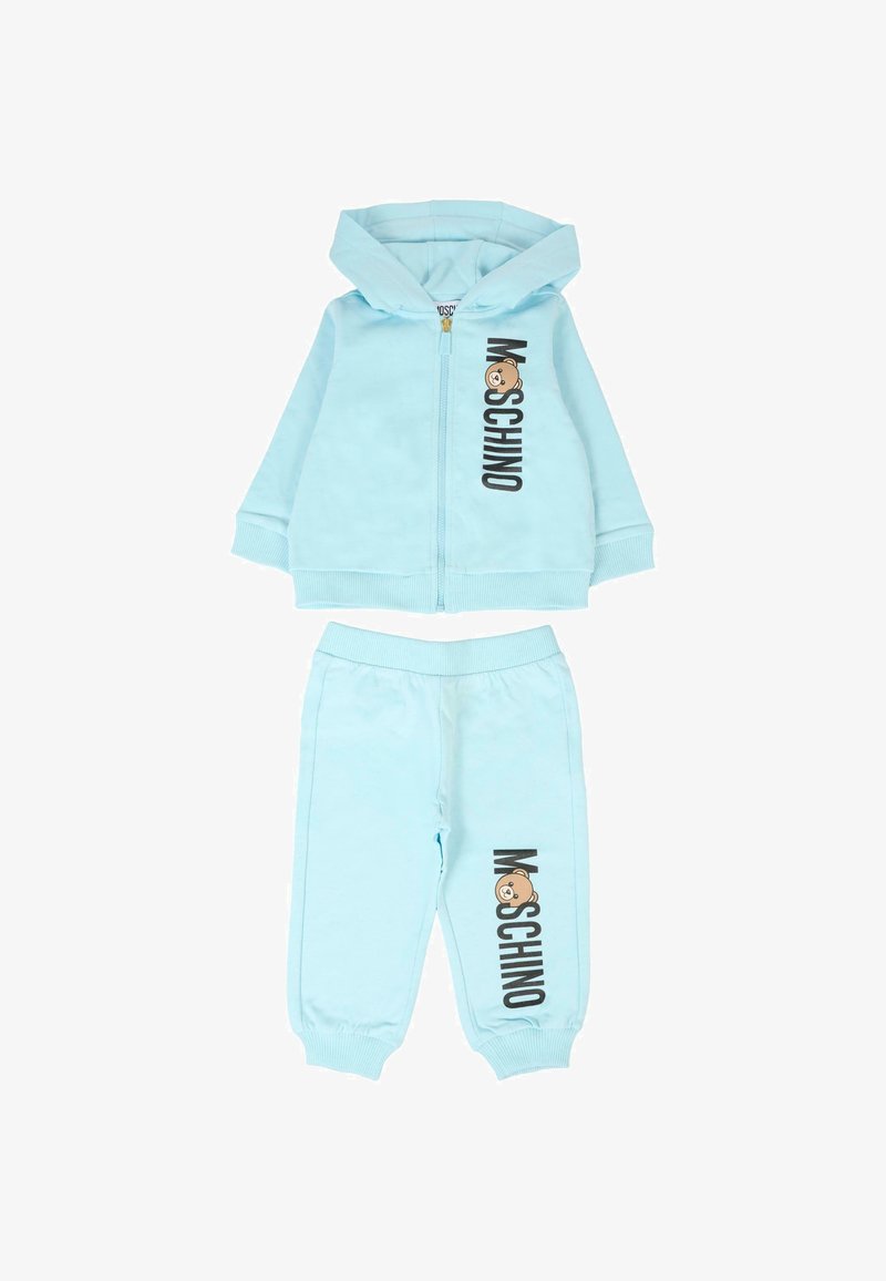 Jasnoniebieski zestaw dresowy z rozpinanym kapturem oraz dopasowanymi spodniami. Posiada logo "Moschino" i grafikę misia. Miękka tkanina, luźny krój.