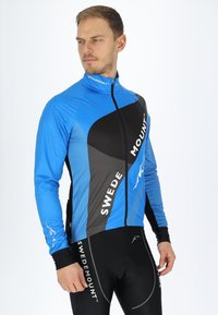 Blauwe fietsjacket met een zwart en grijs ontwerp. Voorzien van een volledige rits en het merklogo aan de voorkant. Materiaal lijkt lichtgewicht en ademend te zijn.