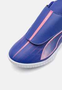 Blue athletic shoe with a smooth synthetic upper, pink accents, textured design, and a white rubber sole. Features a Velcro strap.
