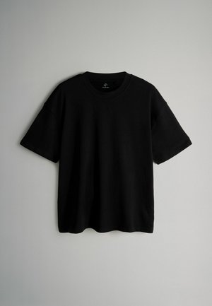 Melna īsām piedurknēm T-kreklā, kas izgatavots no kokvilnas, ar apļa kakla izgriezumu, brīvu piegriezumu un bez redzamām rakstām vai piederumiem. Gluda tekstūra.