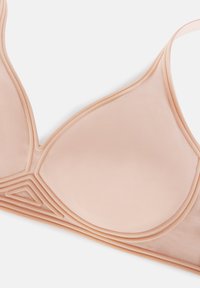 Ljusbeige triangeltopp i slät tyg. Har lager av sömmar längs kanterna och geometriska mönster på kuporna. Mjuk och sömlös design.