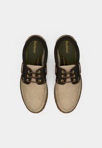 Chaussures marron clair et foncé avec une finition en daim, dotées de lacets marron et d'œillets en métal, conçues dans un style sans lacets et une semelle texturée.