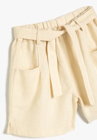 Pantalones cortos de lino en un color beige claro, con una cinturilla elástica, detalle de cinturón de lazo y bolsillos laterales con aberturas en el dobladillo.
