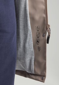 Tuuli- ja vettä hylkivä takki, jossa on harmaa vuori, tummansininen ulkopinta, kaksisuuntainen vetoketju ja huolto-ohjeet painettuna vaaleanruskeaan sisäkerrokseen.