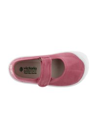 Zapatilla de lona rosa con suela de goma blanca, puntera redonda y una correa en el medio del pie. Presenta un logo en el forro interior.