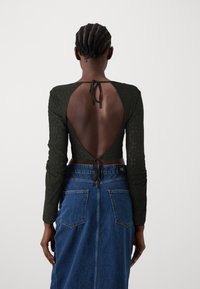 Maglia a maniche lunghe verde scuro con schiena scoperta e fiocco, caratterizzata da un motivo testurizzato. Abbinata a una gonna in denim a vita alta, con un classico colore blu.