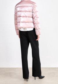 Puffjakke i blank lyserød med horisontalt quiltet design, parret med højtaljede sorte viddebenbukser og spidse sorte hæle.