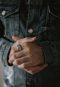 Jeansjacka med metallknappar, händerna hopknäppta, bär en silverring med distinkt detaljer. Strukturerad tyg och sliten utseende.
