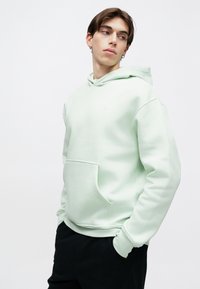 Φούτερ με κουκούλα σε μέντα πράσινο χρώμα, κατασκευασμένο από απαλό ύφασμα, με μπροστινή τσέπη και ρεβέρ στο τελείωμα. Μινιμαλιστικός σχεδιασμός με μικρό λογότυπο στο στήθος.