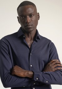 Camisa azul marino con botones, confeccionada en tela suave, con cuello clásico, mangas largas y un sutil detalle de logo en el pecho.