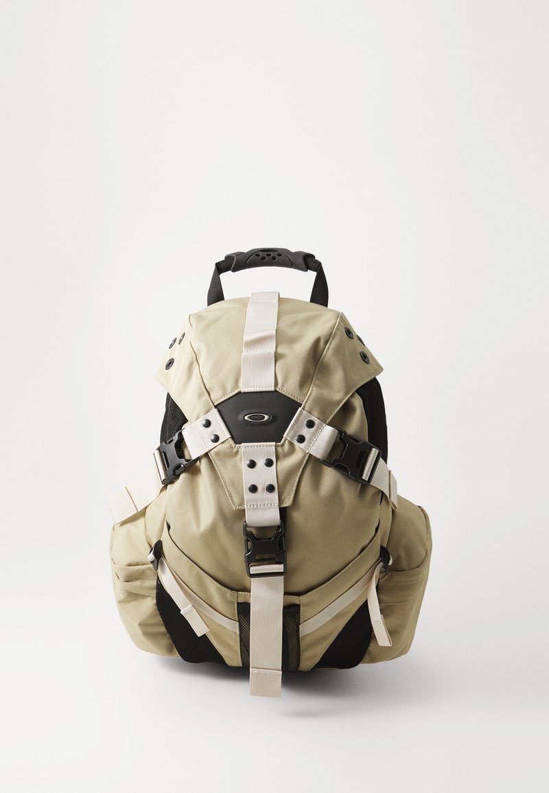 Khakifarbener Rucksack mit schwarzen Akzenten, ausgestattet mit verstellbaren Tragegurten, mehreren Taschen, einem strukturierten Stoff und einem auffälligen Schnallendesign.