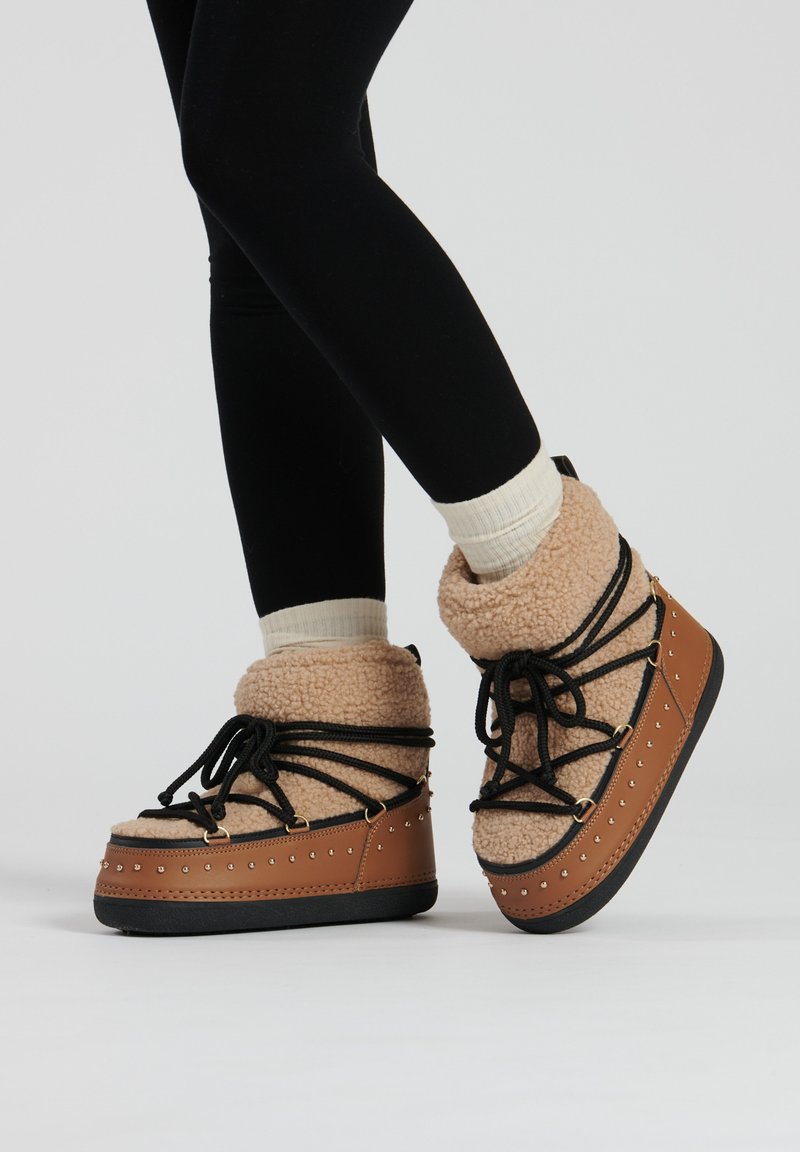 Helle Plattformstiefel mit einem flauschigen beigen Oberteil, schwarzen Schnürsenkeln und Nietenverzierungen entlang der Sohle, kombiniert mit schwarzen Leggings und hellen Socken.