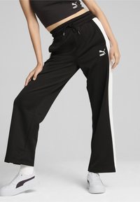 Mustad mustad püksid valgete külgtriipudega, pehmest kangast, millel on elastne vöökoht ja Puma logo vasakul küljel.