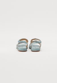 Sandales bleu clair avec une finition en daim, dotées de brides décoratives ornées de strass, semelle plate et design ouvert à l'arrière.