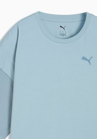 Jasnoniebieska koszulka z krótkimi rękawami, okrągłym dekoltem i subtelnym haftowanym logo na piersi. Gładka, miękka tkanina.