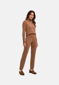 Brązowy dzianinowy sweter z wysokim kołnierzem oraz dopasowane brązowe spodnie, oba wykonane z miękkiego materiału, zestawione z brązowymi mokasynami.