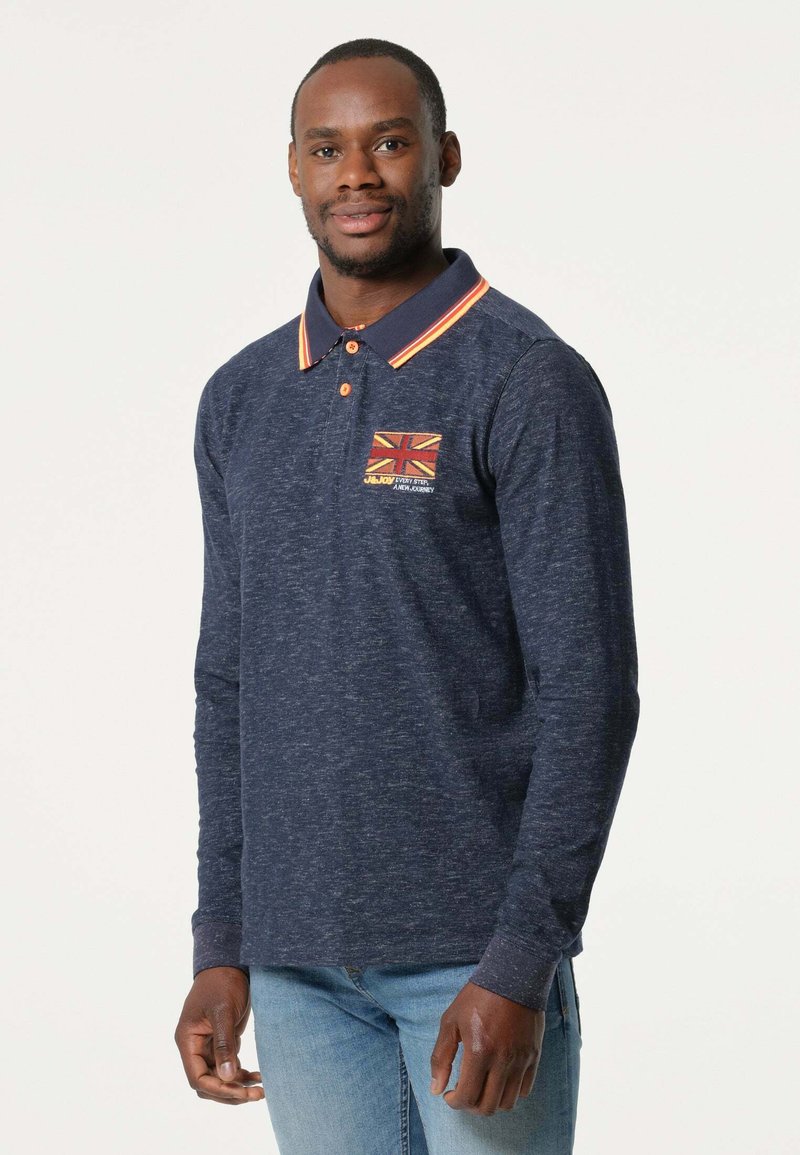 Marineblauwe polo met lange mouwen en oranje accenten, voorzien van een Union Jack-embleem op de linkerborst en een gestructureerde stof.