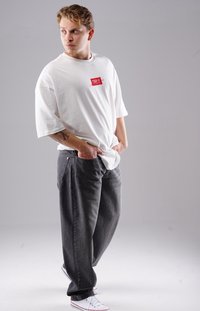Weißes, oversized T-Shirt mit einem roten rechteckigen Patch, kombiniert mit dunkelgrauen, weiten Jeans und weißen Sneakers mit roten Akzenten.