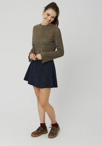 Haut long à manches brunes avec des poignets en volants, associé à une jupe patineuse bleu marine, présentant un tricot texturé. Des chaussures à lacets brunes complètent l'ensemble.