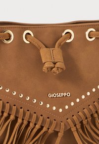 Borsa in suede marrone con hardware dorato, dettagli in frange lungo la parte inferiore e logo impresso. Chiusura con coulisse e nodi decorativi.