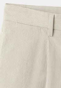 Gros plan d'un tissu beige et blanc à rayures verticales sur un pantalon avec taille et passants de ceinture.