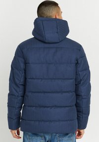 Marineblauer Pufferjacke mit Kapuze, die ein gestepptes Design, gerippte Textur und Seitentaschen aufweist. Aus strapazierfähigem Material gefertigt, ideal für kaltes Wetter.