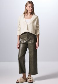 Krémový cardigan, bílý top, olivově zelené široké kalhoty z umělé kůže a huňaté béžové pantofle. Jednoduchý design s detaily na knoflících.