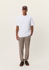 Λευκό κοντομάνικο μπλουζάκι, μπεζ παντελόνι με λεπτές ρίγες, καφέ καπέλο και καφέ παπούτσια. Απλός σχεδιασμός, άνετη εφαρμογή, με ελάχιστες λεπτομέρειες.