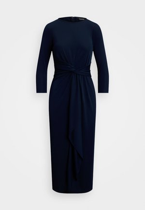 Navy blue, long-sleeve dress in soft fabric, featuring a twisted detail at the waist and a flowing draped front. Concealed zip closure at the back.