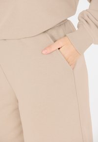 Beiga sweatpants i mjukt material med en sidficka och resårmidja. Texturen är slät med ribbade fållar.