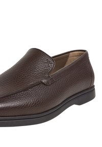 Bruna läder slip-on skor med en texturerad yta, rund tå och en låg svart gummisula; minimal dekorativ sömnadsdetalj.