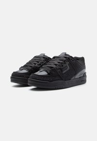 Chaussures de sport noires avec une tige en maille, des accents texturés et des lacets plats. Comprend une semelle rembourrée et des détails en clous métalliques sur l'orteil.